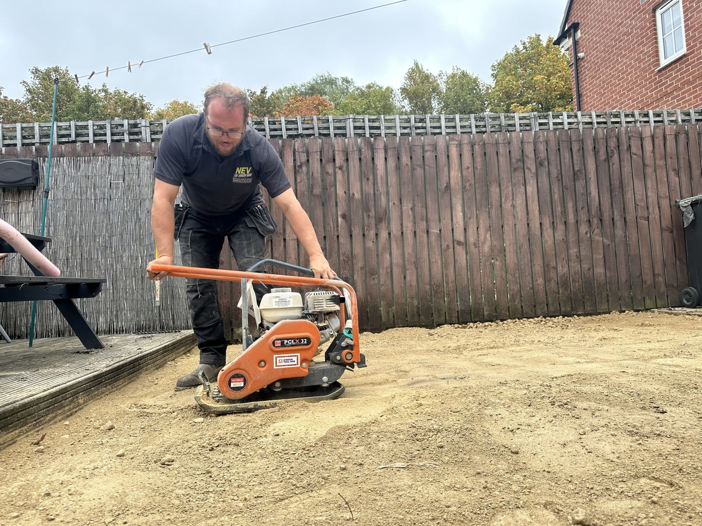 Nev running a plate compactor over the new sub-base along the fence