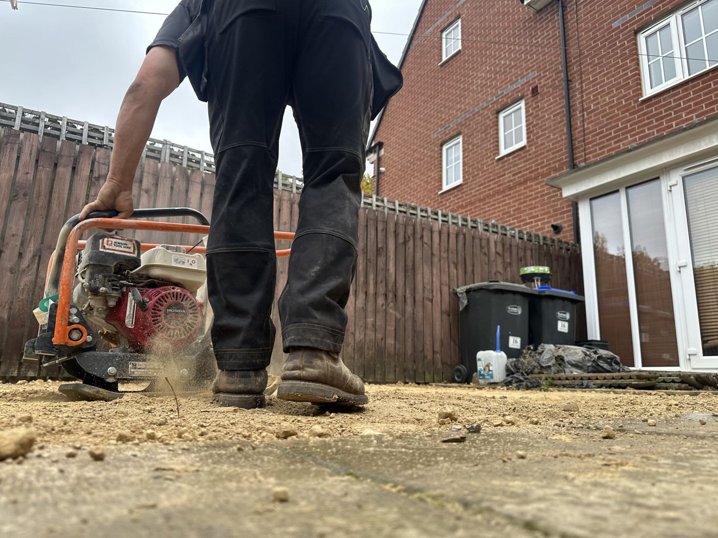 Low view of the plate compactor working the sub-base beside the existing patio slabs