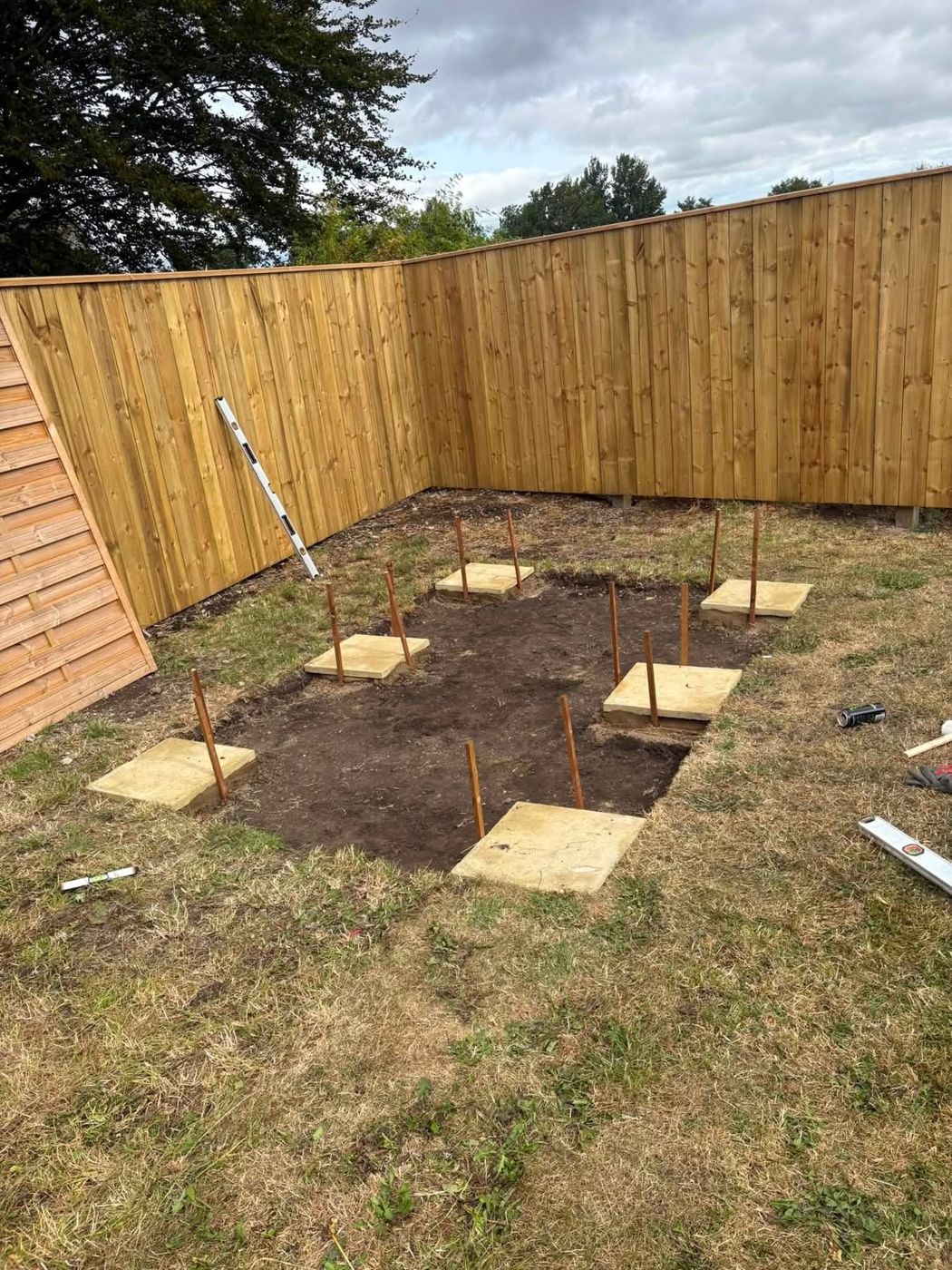 Six paving slabs levelled as a shed base with marker pins